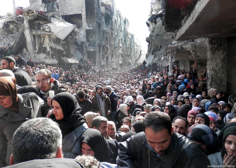 This picture taken on Jan. 31, 2014, and released by the UNRWA, shows residents of the besieged Palestinian camp of Yarmouk, queuing to receive food supplies, in Damascus, Syria. A United Nations official is calling on warring sides in Syria to allow aid workers to resume distribution of food and medicine in a besieged Palestinian district of Damascus. The call comes as U.N. Secretary General Ban Ki-Moon urged Syrian government to authorize more humanitarian staff to work inside the country, devastated by its 3-year-old conflict. (AP Photo/UNRWA)